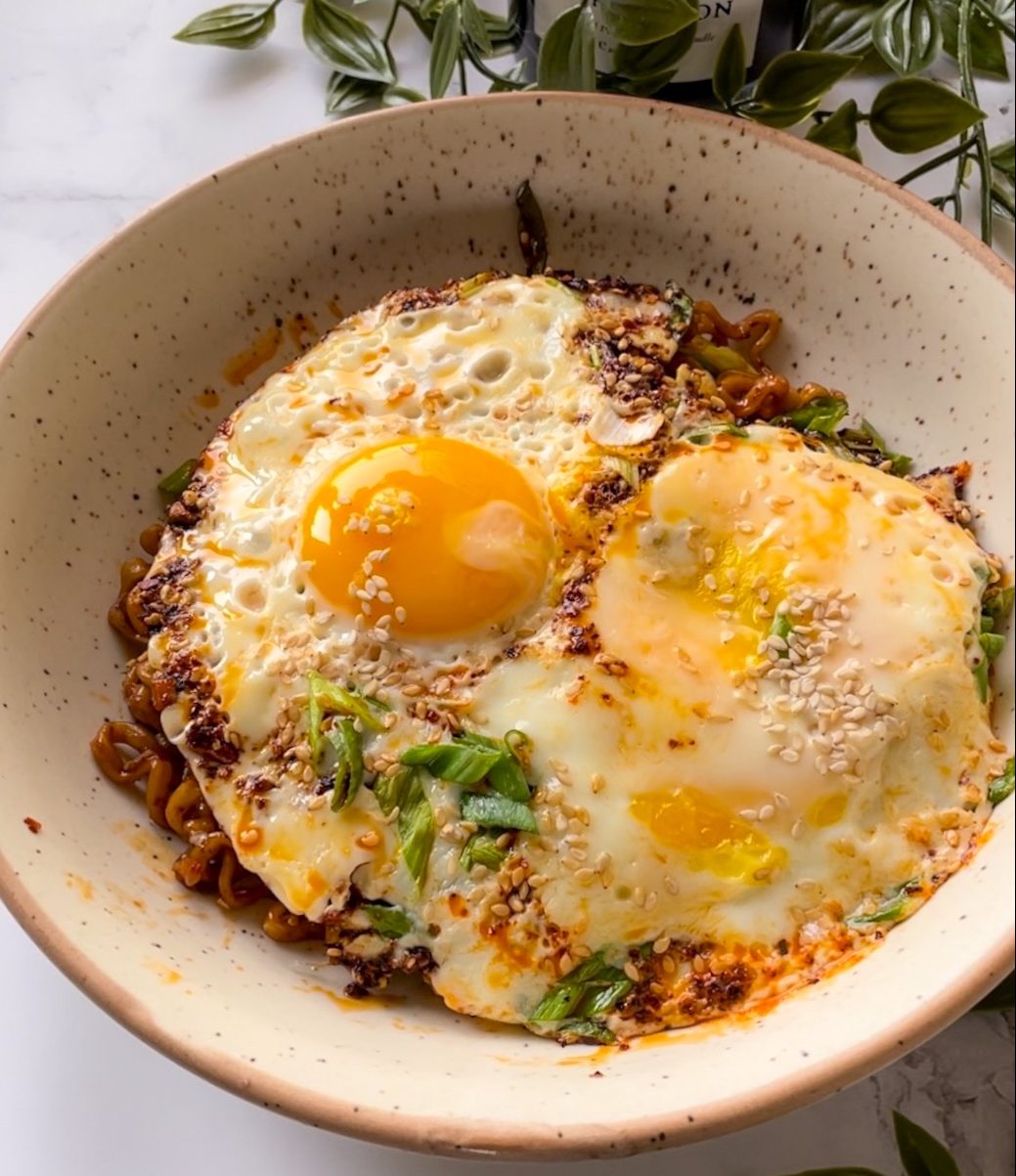 Fried eggs over noodles, finished with chili oil, sesame, and spring onion