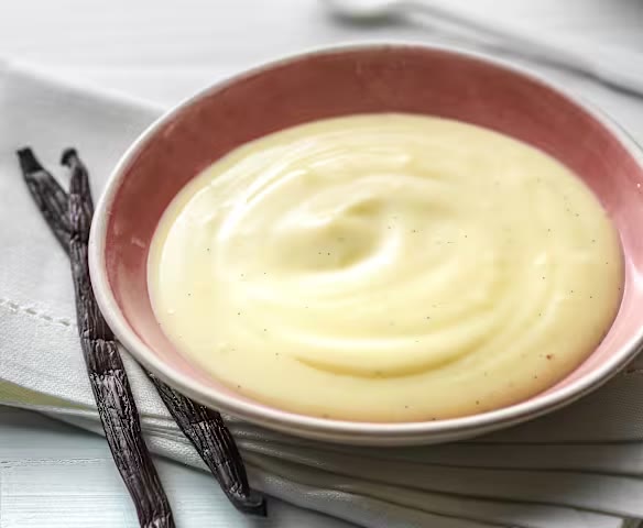 Silky vanilla custard in a bowl beside whole vanilla pods